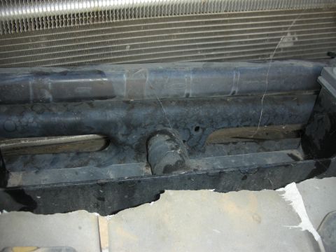 2004 Ford Crown Victoria - Close-up looking down at the front of a vehicle with the radiator core support area exposed, showing an aluminum radiator or condenser core…