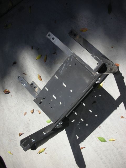 2004 Ford Crown Victoria - Overhead shot of a bare push-bumper assembly resting upside down on leaf-strewn concrete, showing its slotted flat center license/mount pla…