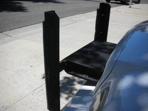2004 Ford Crown Victoria - A black-painted push bumper standing on a sunlit sidewalk with its two channel uprights and drilled flat center mounting plate facing the c…