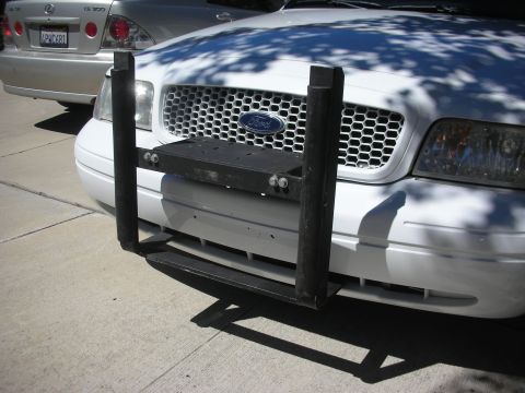 2004 Ford Crown Victoria - Close-up of a white Ford Crown Victoria front with black push-bar bracket; silver Lexus IS with plate ABC681 parked beside it.