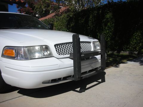 2004 Ford Crown Victoria - Front three-quarter view of a white Ford Crown Victoria sedan with a heavy-duty black steel push bumper/bull bar mounted to the front, park…