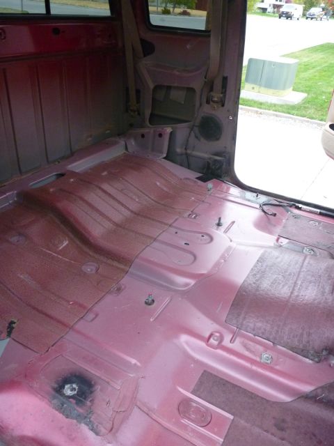 1997 Dodge 2500 - The interior of a red pickup truck is shown with the flooring removed, revealing the metal structure underneath.