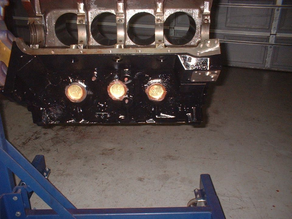 Black engine block on a blue stand, showing cylinder bores and oil galley plugs