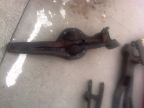 1986 Ford Bronco - A dark-colored rear axle assembly is shown lying on a concrete surface, with other parts visible in the background.