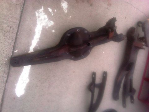 1986 Ford Bronco - Rear axle housing and associated suspension parts laid out on a concrete surface.