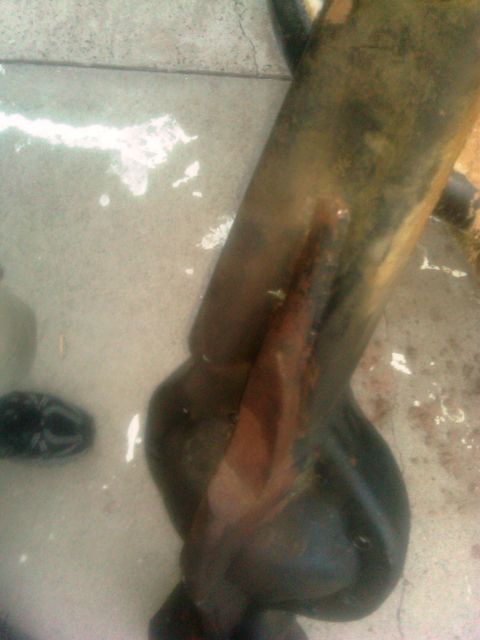 1986 Ford Bronco - A close-up view of a heavily corroded vehicle suspension part resting on wet concrete.