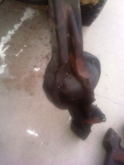 1986 Ford Bronco - A close-up view of a dark, possibly rusted, automotive suspension component resting on a concrete floor.
