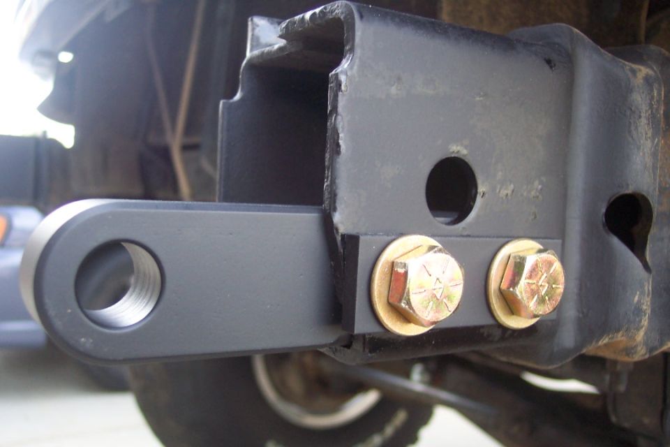 Trailer hitch receiver with two gold bolts attached to a black frame. A circular metal loop extends from the receiver