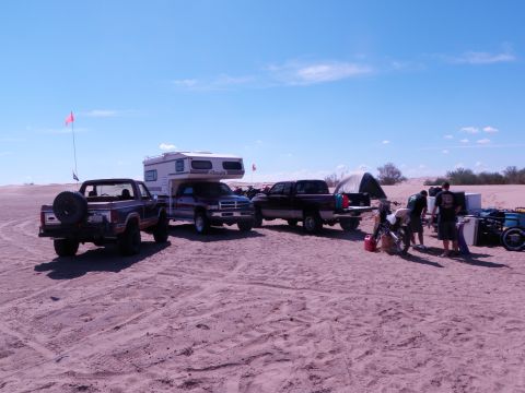1982 Ford Bronco - Several vehicles are parked on a sandy terrain under a clear blue sky.