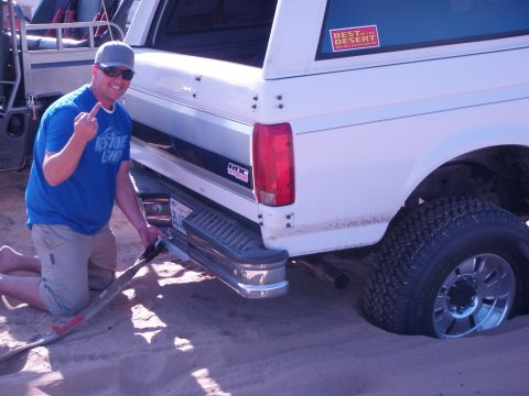 1982 Ford Bronco - A man attempts to free a white Ford Bronco stuck in the sand, with a "Best in the Desert" sticker visible on the rear window.