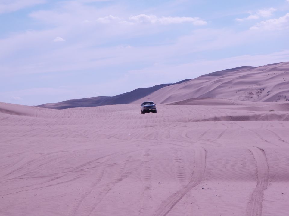 Truck driving on sand dunes under a cloudy sky