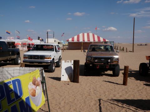 1982 Ford Bronco - Two Ford Broncos are parked on the sand in front of a tent.