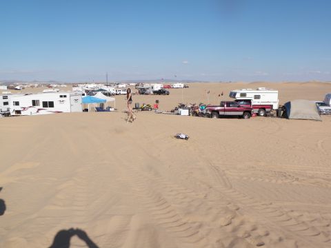 1982 Ford Bronco - A busy desert campsite scene features numerous recreational vehicles, campers, and trucks parked on the sand under a bright, clear sky.