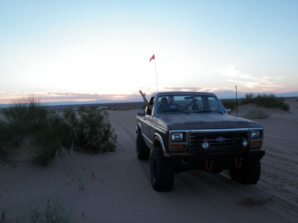 Brown pickup truck with a red flag driving in the desert at sunset