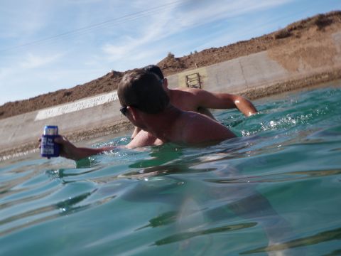 1982 Ford Bronco - Two people swim in a canal, with a concrete embankment and brown hills in the background.