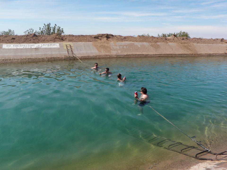 People swim in a canal with a 'No Trespassing' sign on the bank