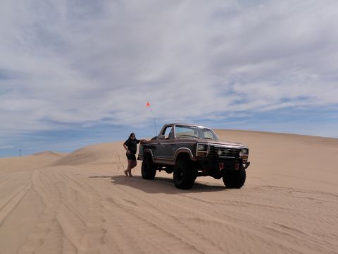1982 Ford Bronco - A person stands next to a lifted Ford F-Series truck in a sandy desert landscape under a cloudy sky.