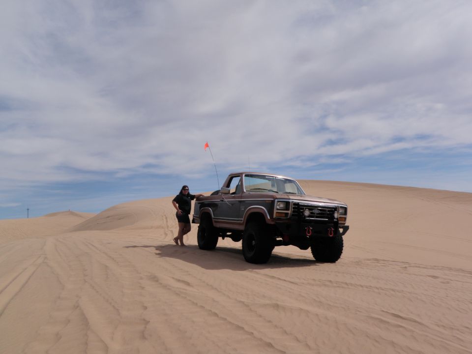 Ford F-Series truck parked on sand dune with person leaning on it