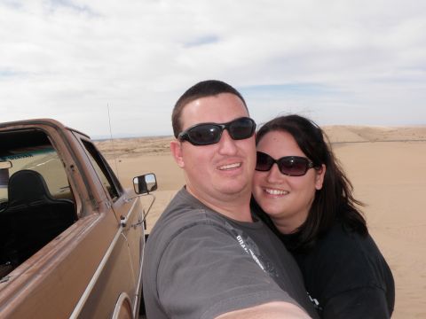 1982 Ford Bronco - Couple poses for a selfie in front of a brown truck in a desert landscape.