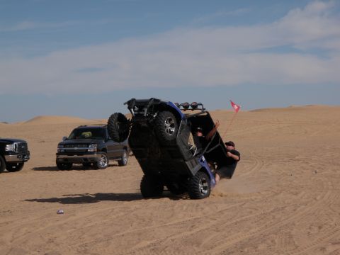1982 Ford Bronco - An off-road vehicle has flipped over in the sand dunes, with occupants attempting to right it.