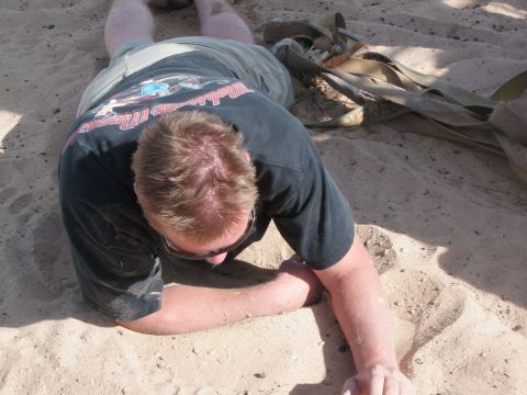 1982 Ford Bronco - A person is lying face down in the sand with a tow strap next to them.