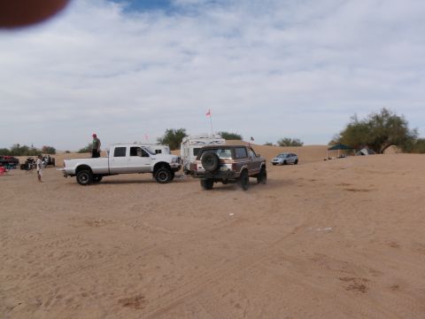 1982 Ford Bronco - A brown Ford Bronco is parked in the sand dunes next to a white pickup truck and a trailer.