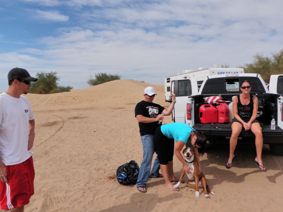 Desert scene with people, dog, pickup truck, and RV