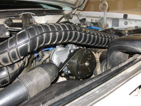 1995 Ford Bronco - Close-up of an engine bay, focusing on the air conditioning compressor and a large, ribbed intake hose.