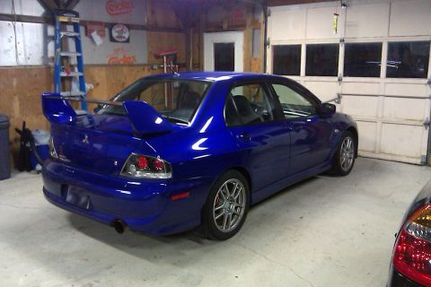 2006 Mitsubishi Evolution - A blue 2006 Mitsubishi Evolution VIII is parked in a garage, showing its distinctive rear spoiler and taillights.