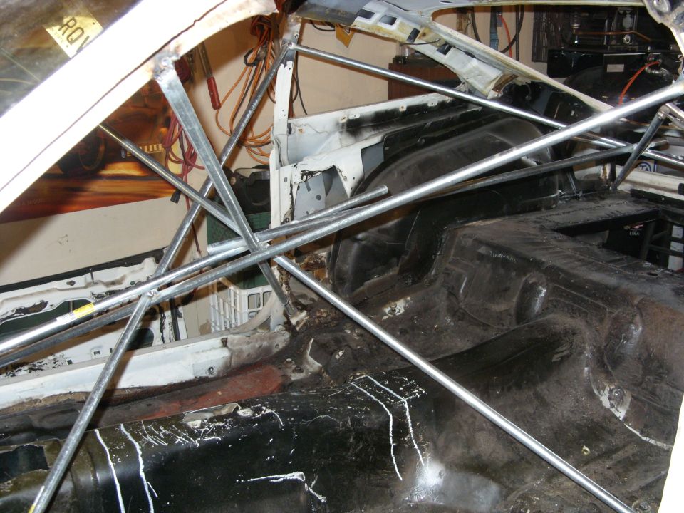 Car interior stripped down with a metal roll cage installed. Floor is dirty and shows rust