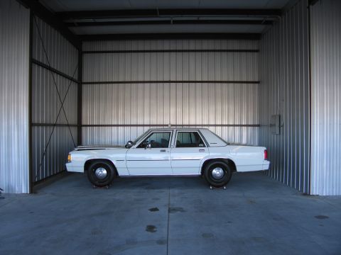 1991 Ford LTD Crown Victoria - Side view of a white sedan parked inside a metal structure.