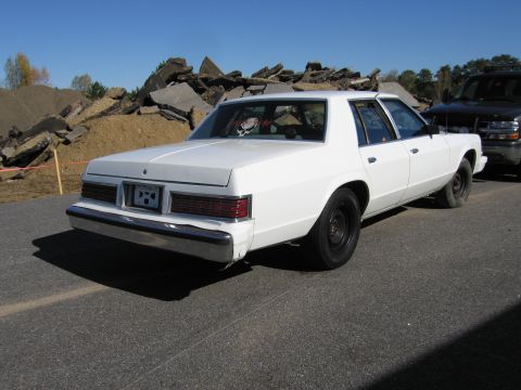 1991 Ford LTD Crown Victoria - Rear view of a white sedan with black steel wheels, parked near a pile of debris.