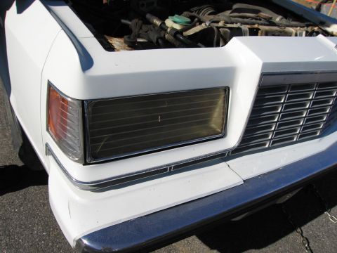 1991 Ford LTD Crown Victoria - Close-up of a car's front end, revealing the grille and headlight assembly with the hood open.