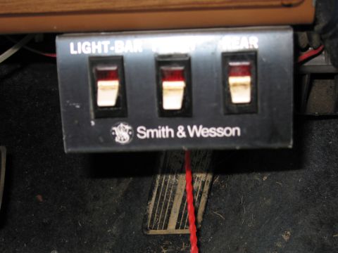 1991 Ford LTD Crown Victoria - A Smith & Wesson control panel with three switches is mounted in a vehicle's interior.