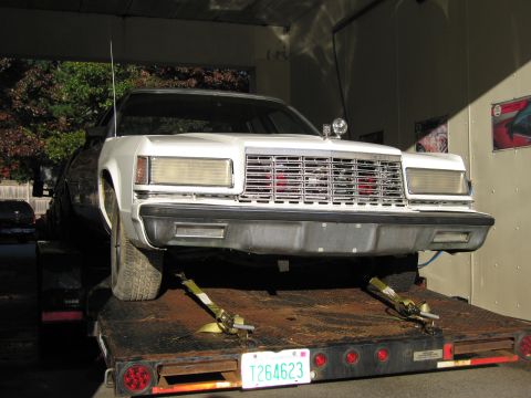 1991 Ford LTD Crown Victoria - White 1980s Ford sedan being transported on a car hauler trailer.