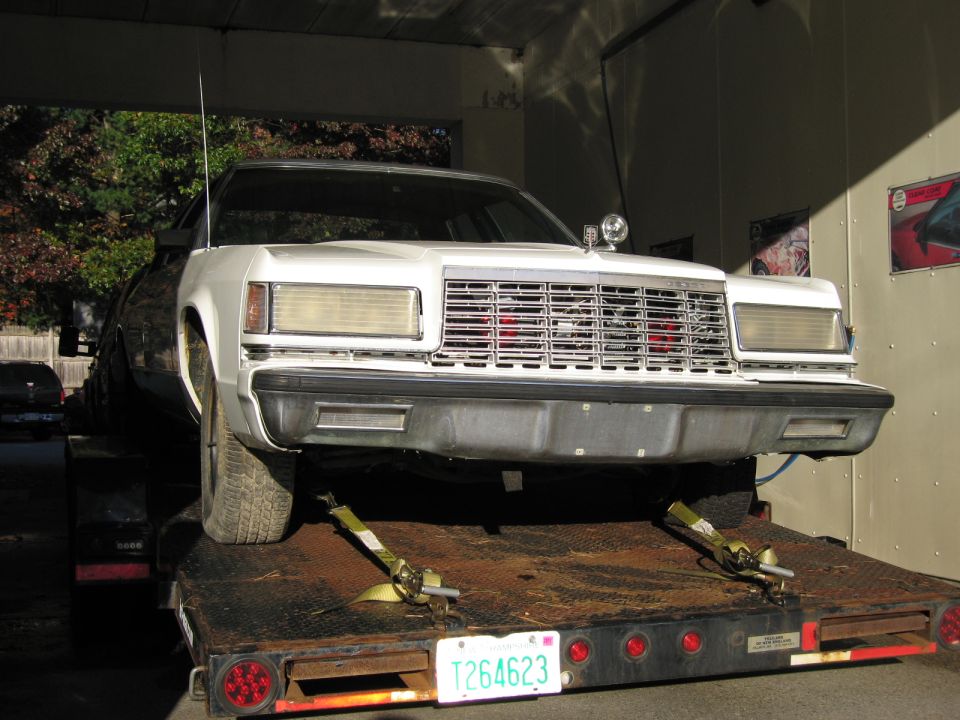 Front view of a white 1980s Ford sedan on a car hauler trailer. License plate T264623