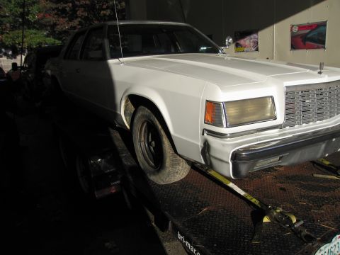 1991 Ford LTD Crown Victoria - A white sedan is secured to a trailer, viewed from the front right side.