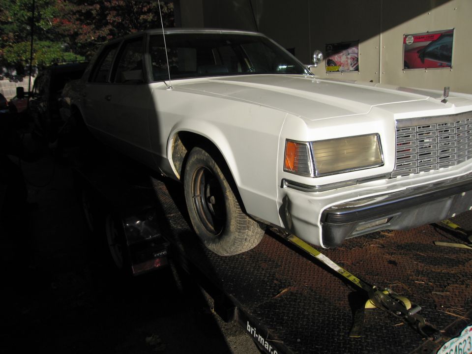 White sedan on a trailer, front quarter view, showing a large chrome grille and rectangular headlights