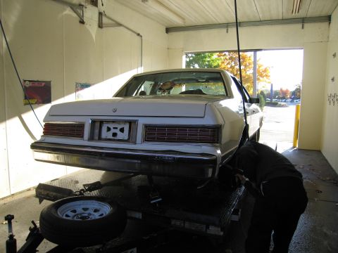 1991 Ford LTD Crown Victoria - A person works on the rear of a white sedan that is raised on a lift inside a garage.