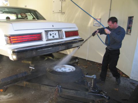 1991 Ford LTD Crown Victoria - A man washes the rear of a white sedan that is on a trailer, with a spare tire on the trailer bed.