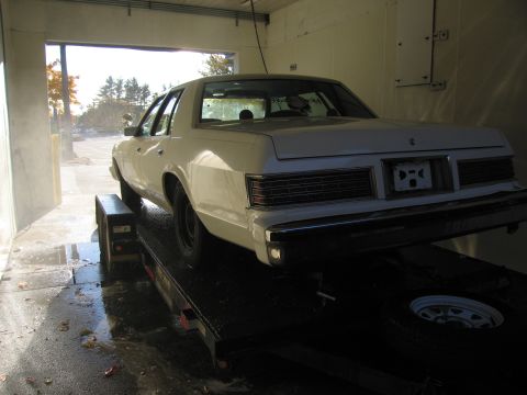 1991 Ford LTD Crown Victoria - White sedan on a trailer, rear view. Grille and taillights suggest late 1970s model.