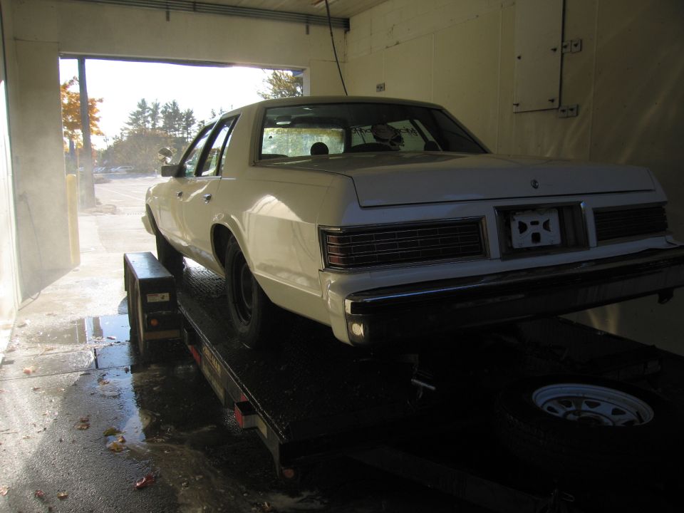 White sedan on a trailer, rear view. Grille and taillights suggest late 1970s model