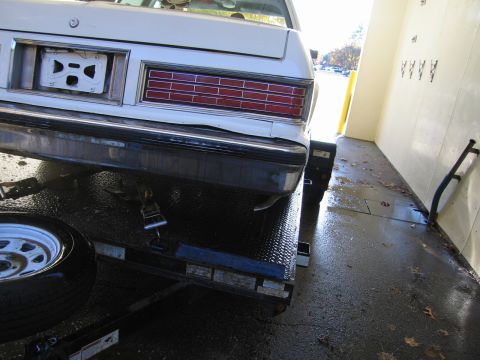 1991 Ford LTD Crown Victoria - Rear view of a white car being transported on a trailer, showing the bumper and taillight assembly. The year is estimated to be 1991.