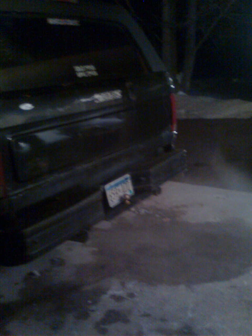 Rear view at night of a dark SUV with license plate on bumper, trailer hitch ball, parked on snowy ground