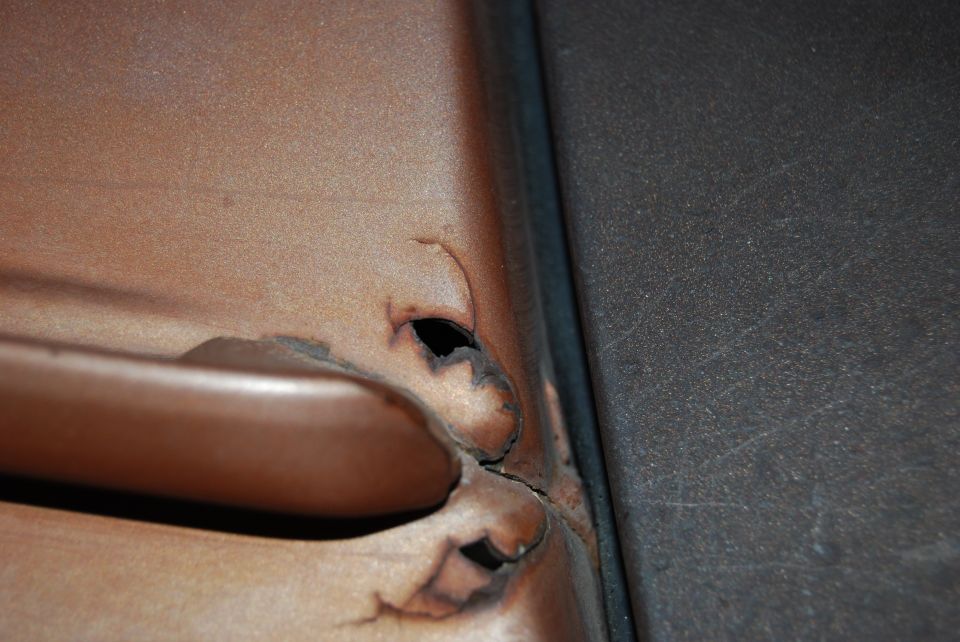 close-up of rust and holes around a door handle on a vehicle