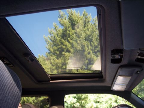 2006 Chevrolet Corvette - View through an open sunroof shows green trees and a blue sky, with interior car elements visible.