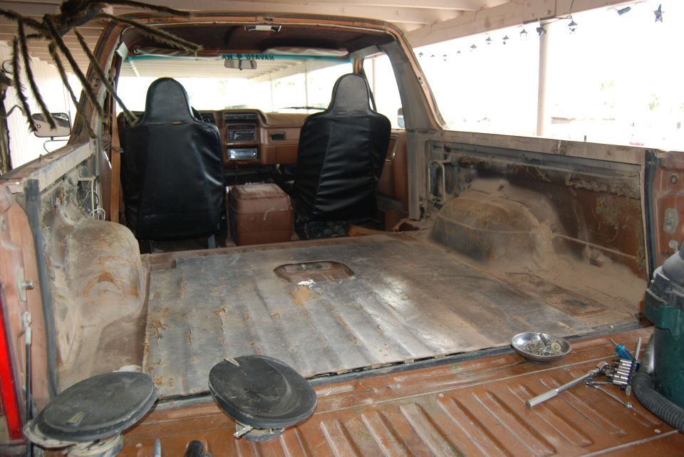 Interior view of a truck bed with seats and dashboard visible. Some tools and a bowl of screws are in the bed