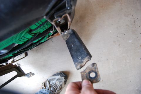 1982 Ford Bronco - A person holds a broken seat bracket, revealing the underside of a seat with green fabric.