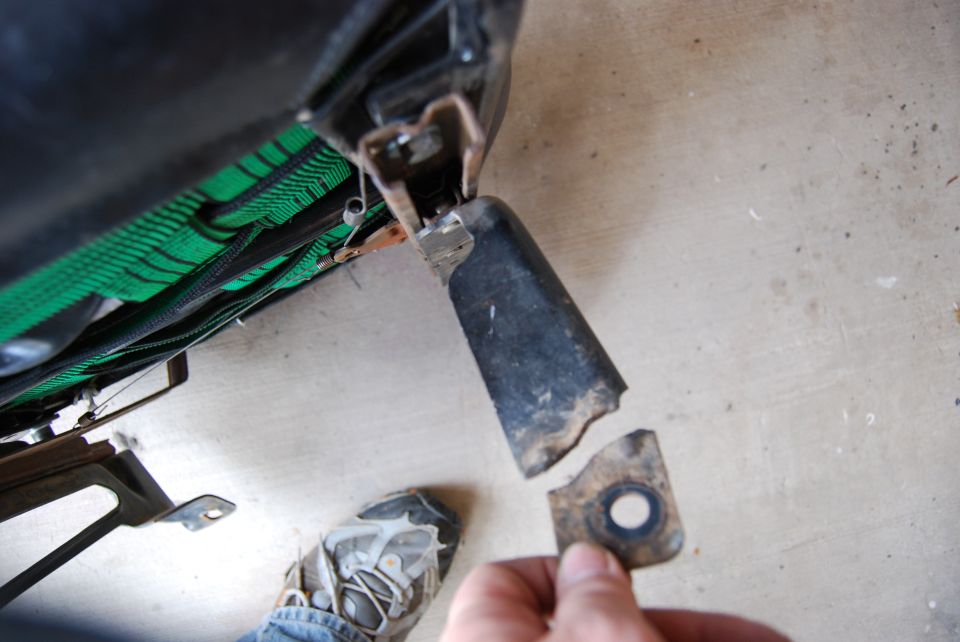 Close-up of a broken metal seat bracket being held, with green seat fabric visible