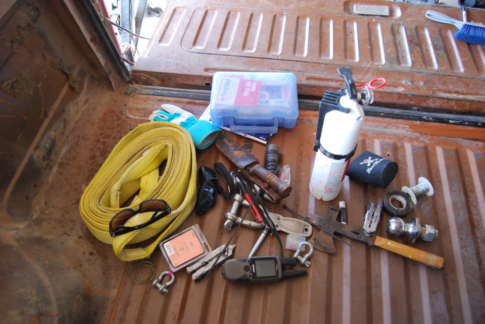 Truck bed with yellow tow strap, first aid kit, fire extinguisher, tools, and GPS device